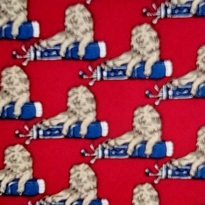 May include: A red fabric with a repeating pattern of white lions sitting on blue golf bags. The lions are facing right and have a playful expression.
