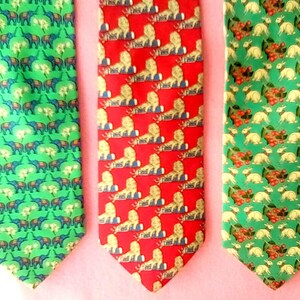 May include: Three silk neckties with different patterns. The first tie has a green background with a repeating pattern of elephants and flowers. The second tie has a red background with a repeating pattern of lions and flowers. The third tie has a green background with a repeating pattern of rabbits and flowers.