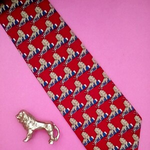 May include: A red silk tie with a repeating pattern of white lions on a blue background. The tie has a pointed end and is made of a smooth, luxurious fabric.