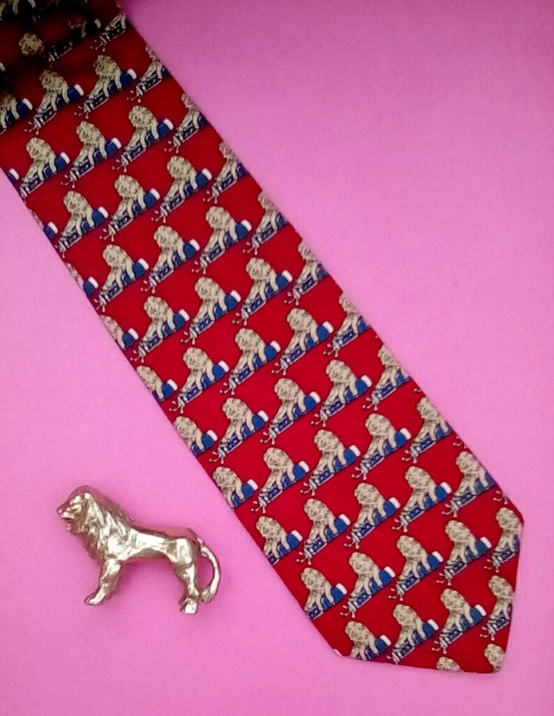 May include: A red silk tie with a repeating pattern of white lions on a blue background. The tie has a pointed end and is made of a smooth, luxurious fabric.