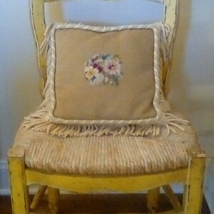 May include: A yellow painted wooden chair with a woven seat and a cream-colored pillow with a floral embroidery design.