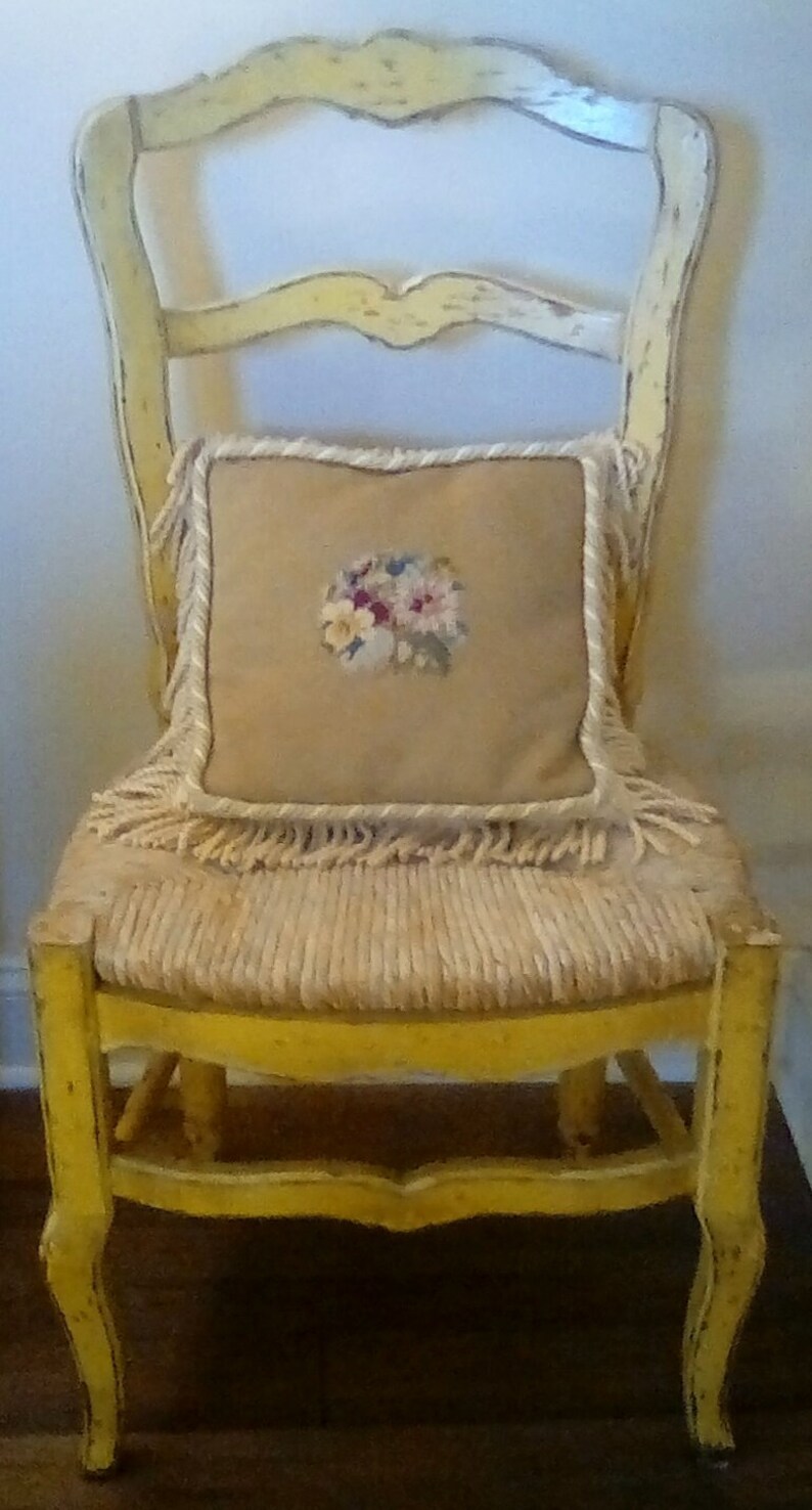 May include: A yellow painted wooden chair with a woven seat and a cream-colored pillow with a floral embroidery design.