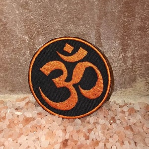 May include: Orange embroidered Om symbol patch on a black circular background.