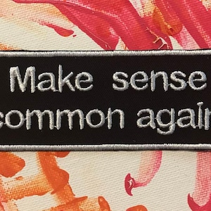 May include: Black patch with white embroidered text that reads "Make sense common again".