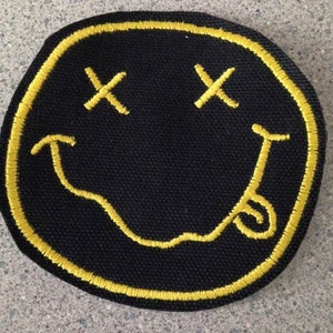 May include: Black and yellow embroidered smiley face patch with an 'X' for eyes and a crooked smile.
