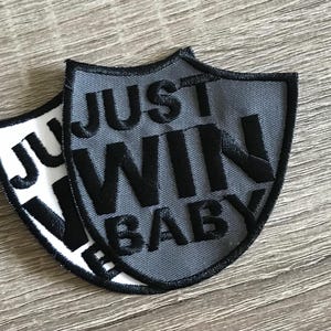 May include: Two gray and white embroidered patches with the text "Just Win Baby" in black.