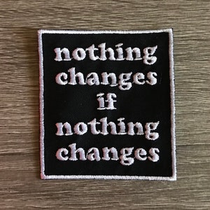 May include: Black embroidered patch with white text that reads "nothing changes if nothing changes".