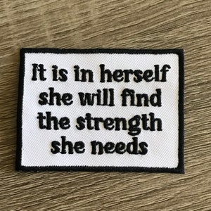 May include: White fabric patch with black embroidered text that reads "It is in herself she will find the strength she needs".