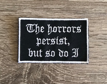 May include: Black embroidered patch with white text that reads "The horrors persist, but so do I."