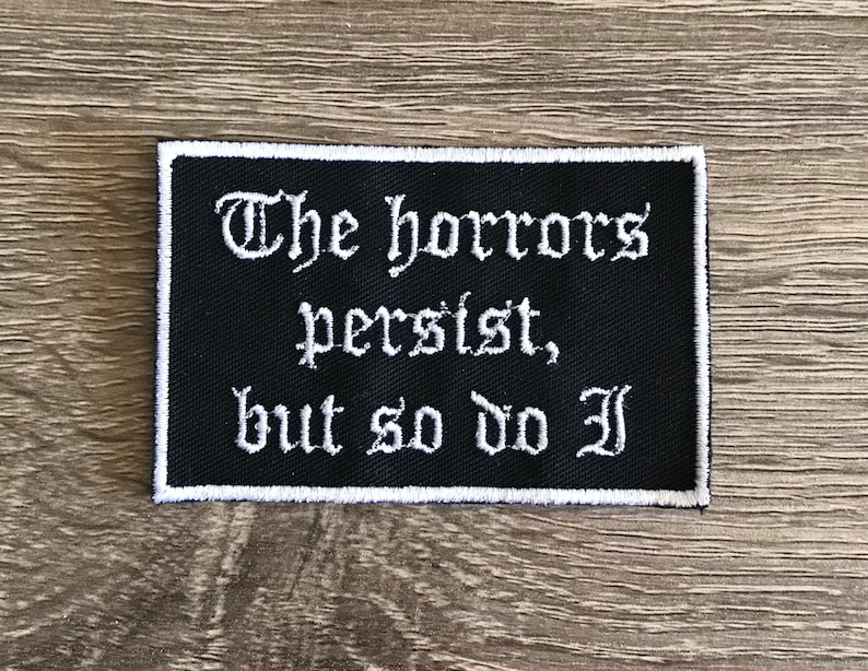 Puede incluir: Parche bordado negro con texto blanco que dice "The horrors persist, but so do I."