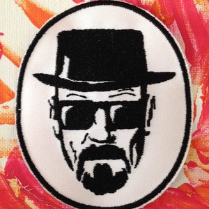 May include: Black and white embroidered patch of a man's face wearing a hat and sunglasses. The background is white.