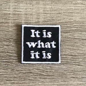May include: Black and white embroidered patch with the text "It is what it is" on a black background.