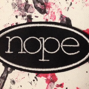 May include: Black oval patch with white stitching and the word "nope" in white lettering.