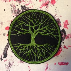 May include: A green tree of life embroidered patch on a black background. The patch is circular and has a detailed design of a tree with roots and branches.