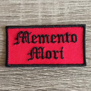 May include: Red rectangular embroidered patch with black stitching and the text "Memento Mori" in a gothic font.