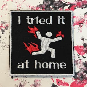 May include: Black and white embroidered patch with red flames. The patch says "I tried it at home".