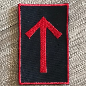 May include: Red embroidered arrow pointing upwards on a black fabric patch with a red border.