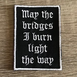 May include: Black fabric patch with white embroidered text that reads "May the bridges I burn light the way".