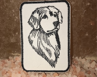 May include: A white embroidered patch with a black line drawing of a dog's head. The dog is looking to the right and has a short, fluffy coat.