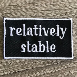 May include: Black fabric patch with white embroidered text that reads "relatively stable".