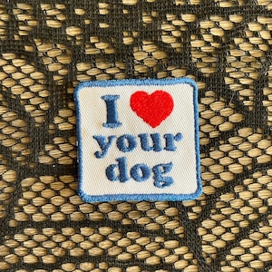 May include: A square patch with a white background and a blue border. The patch features the phrase "I ❤️ your dog" in blue letters, with a red heart replacing the word "love".