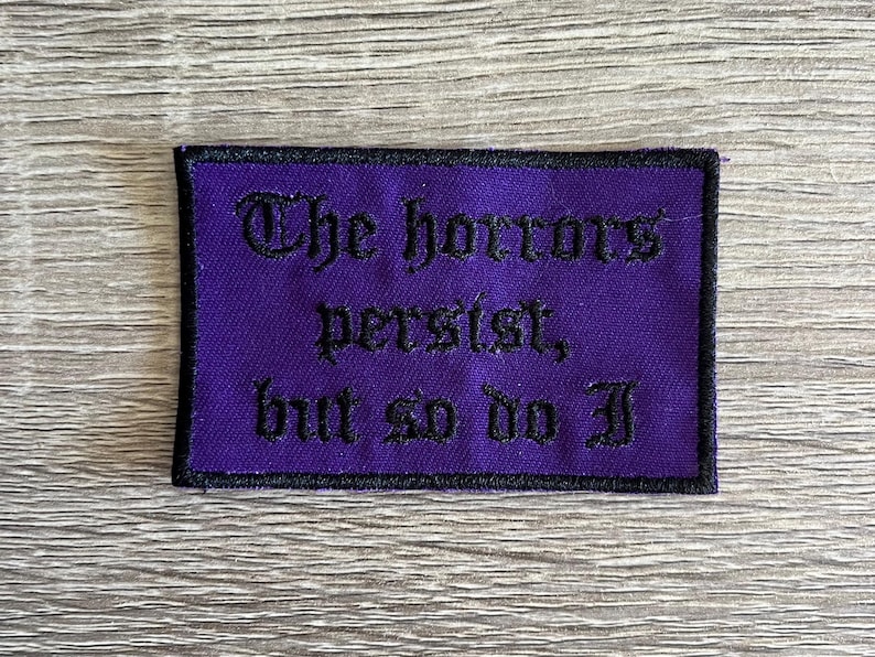 Puede incluir: Parche bordado morado con texto negro que dice "The horrors persist, but so do I."