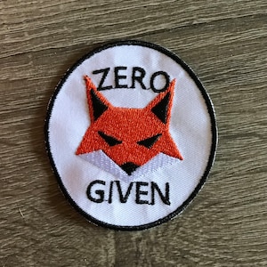 May include: Embroidered patch with a white background, black border, and the words "ZERO GIVEN". The patch features a stylized orange fox with black accents.