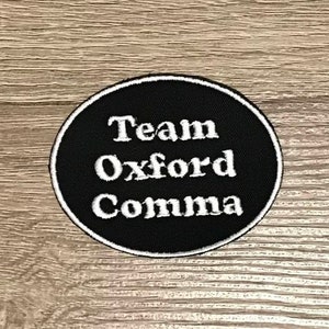 May include: Black and white circular patch with the text "Team Oxford Comma" in white.