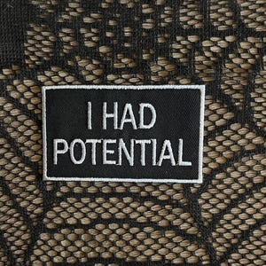 May include: A rectangular black embroidered patch with a white border and the white text I HAD POTENTIAL stitched in a clean sans-serif font. The patch features a tight, uniform thread density and a crisp, defined edge for clear readability.