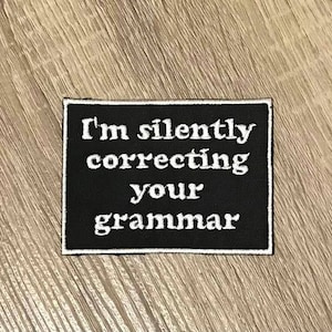 May include: Black and white embroidered patch with the text "I'm silently correcting your grammar".