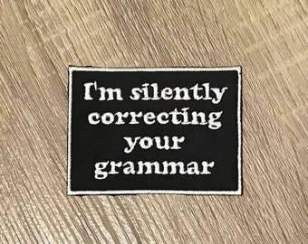 May include: Black and white embroidered patch with the text "I'm silently correcting your grammar".