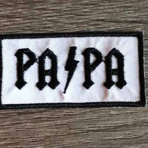 May include: White embroidered patch with black lettering that reads "PA/PA" in a gothic font.
