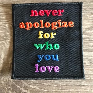 May include: A black embroidered patch with the text "never apologize for who you love" in rainbow colors.
