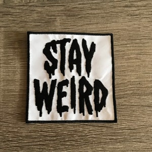 May include: White fabric patch with black embroidered text that reads "STAY WEIRD".