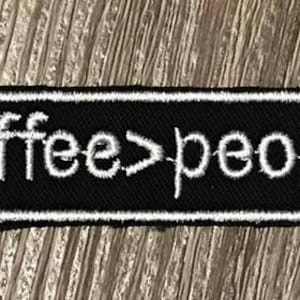 May include: Black and white embroidered patch with the text "coffee>people" on a white background.