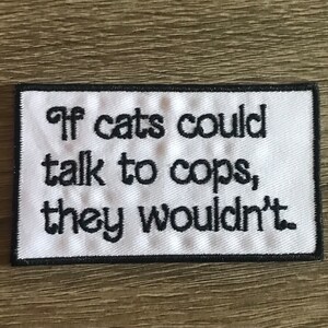 May include: White embroidered patch with black text that reads "If cats could talk to cops, they wouldn't."