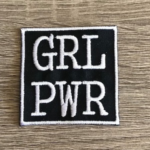 May include: Black and white embroidered patch with the text "GRL PWR" in white lettering.
