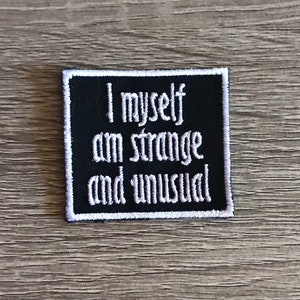 May include: Black embroidered patch with white stitching. The patch reads "I myself am strange and unusual".