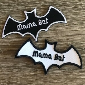 May include: Two bat-shaped patches. One is black with white trim and the words "Mama Bat" in white script. The other is white with black trim and the same text. Both are embroidered.