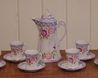 May include: A vintage tea set with a white teapot and six cups and saucers. The teapot has a floral design with pink and purple roses. The cups and saucers have a similar floral design.