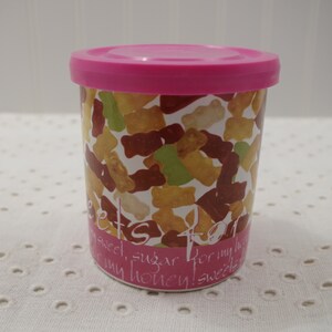 May include: A pink plastic container with a lid, filled with colorful gummy bears. The container has a white background with the text "Sweet for my honey! Sweets, sweet, sugar, darling, honey!" printed on it.