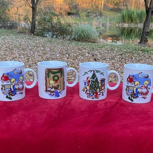 May include: Set of four white ceramic mugs with Christmas scenes. Each mug features a different scene with a house, a Christmas tree, and children. The mugs have blue, red, green, and yellow accents.