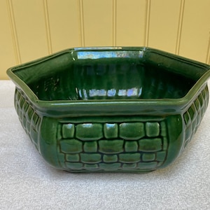 May include: A green ceramic planter with a hexagonal shape and a brick-like pattern around the rim.