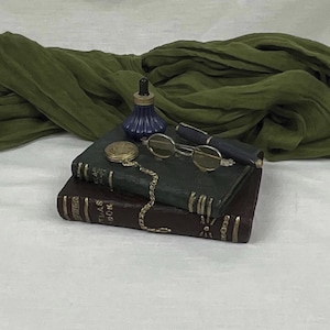 May include: Two leather-bound books with gold accents, a blue glass bottle with a stopper, a pair of round glasses, and a gold chain with a pocket watch.