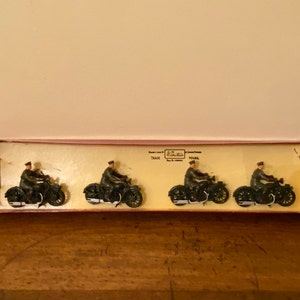 May include: Four toy motorcycles with riders in a box. The motorcycles are green and black, and the riders are wearing green uniforms. The box is red and white and has the text "Corgi Toys Made in Gt. Britain" on it.