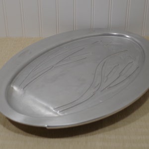 May include: A silver oval serving tray with an embossed design of stylized leaves. The tray is made of metal and has a smooth, polished finish.