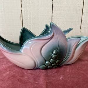 May include: A ceramic planter shaped like a flower with pink and green glaze. The planter has a wide, shallow bowl and a raised center with a flower bud design.