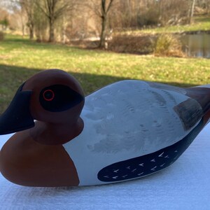 Puede incluir: Un señuelo de pato de madera pintado a mano con pintura marrón, blanca y negra. El pato tiene un pico negro y ojos rojos.