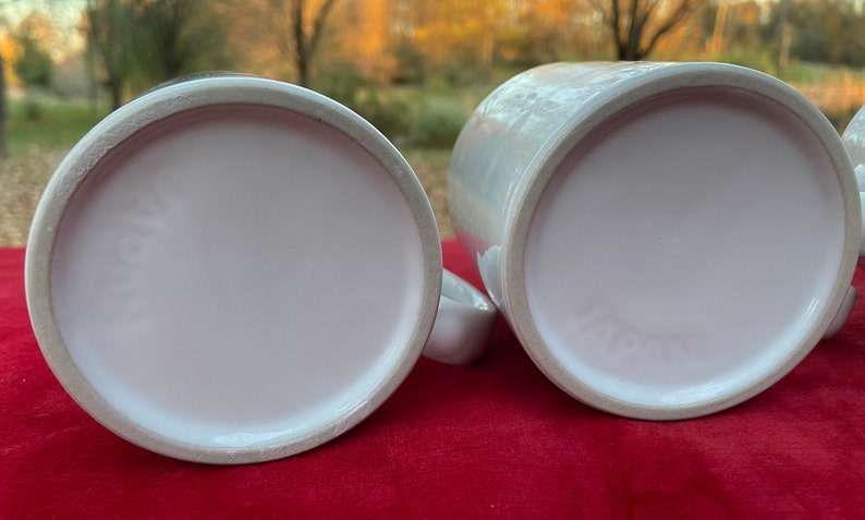 May include: Two white ceramic mugs with a smooth, glossy finish. The mugs are empty and have a light pink interior.