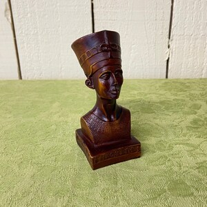 May include: A dark brown wooden bust of an Egyptian pharaoh wearing a headdress with a decorative design. The bust is on a rectangular base with the word "Egypt" inscribed on it.